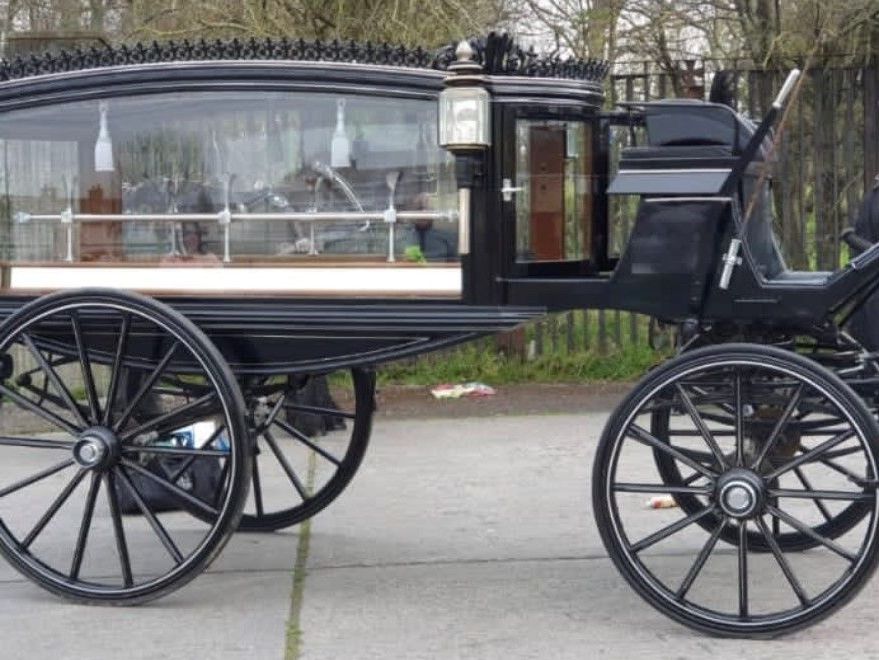 A parked black horse drawn funeral carriage