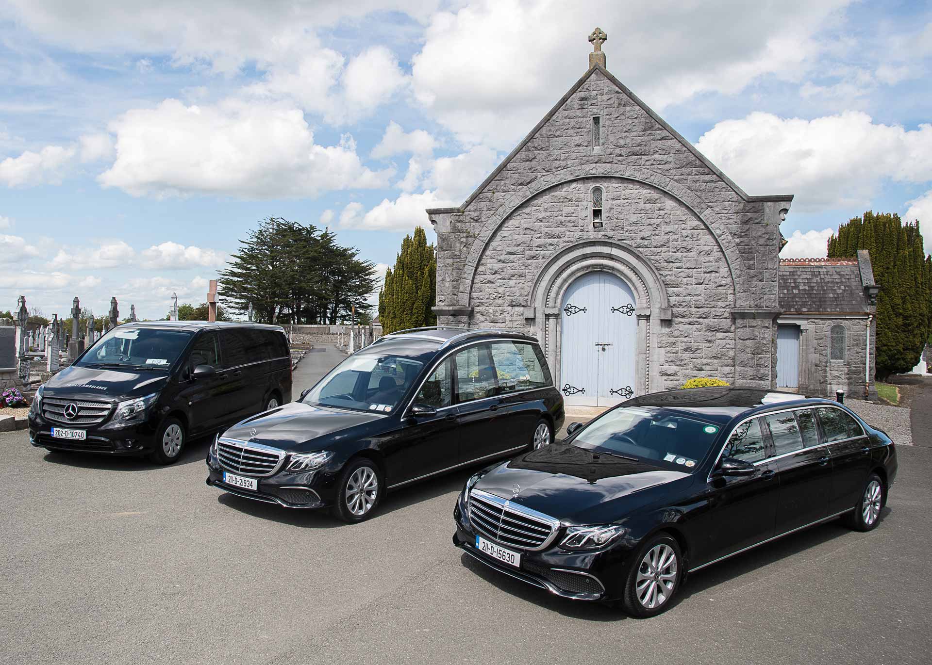 Black limousine, black minibus and a black hearse outside a church