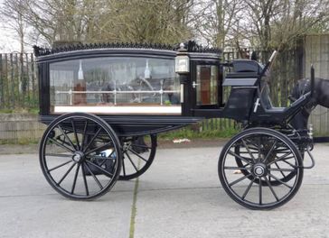 A side angle of a black horse drawn Hearse