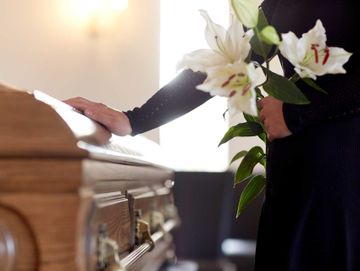 A person paying their respects by placing a hand on a coffin